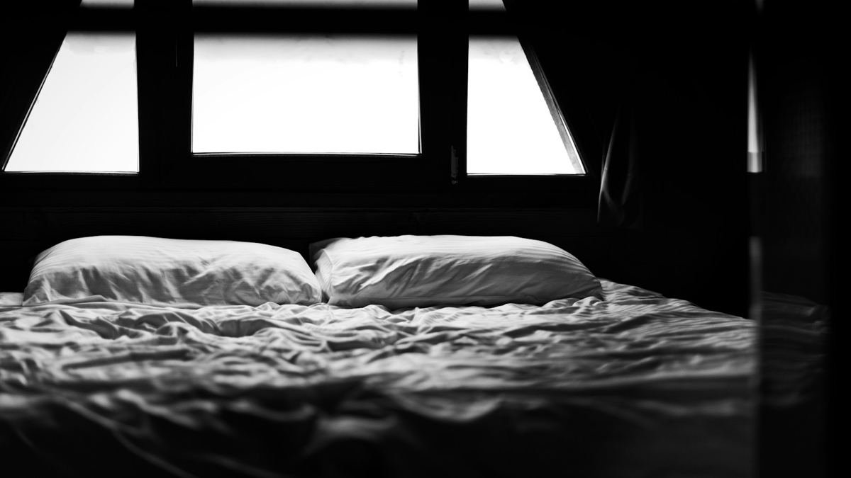 Dark bedroom with an empty bed and a bright window